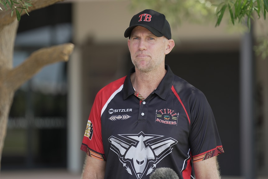 Mid shot of a man wearing a red and black sports club shirt.