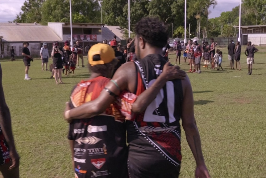 Two football players with their arms around each other's shoulders walking on the field.