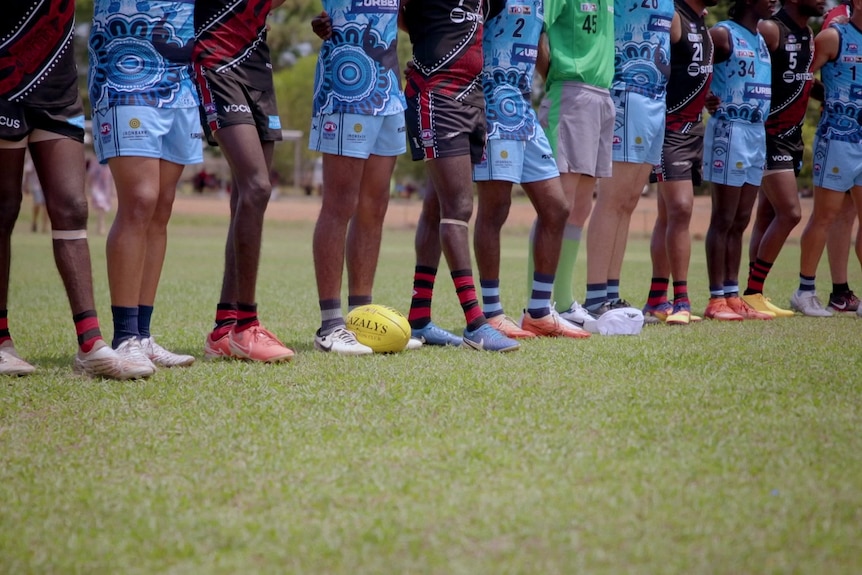 Two opposing footy teams standing in a line on the field.