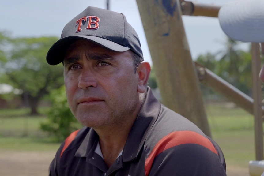 Man in a black cap with the letters TB embroidered on it, wearing a black shirt with red stripes.