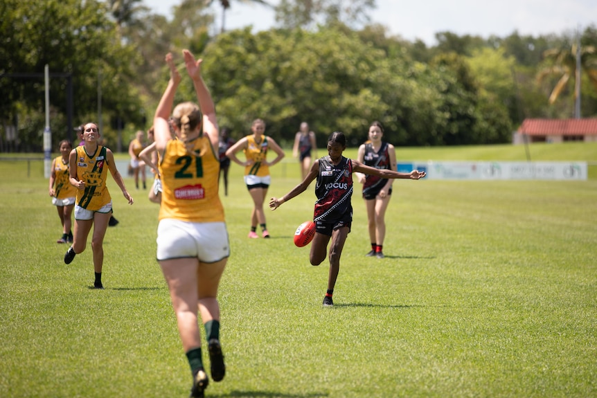 A woman playing Australian Rules football in a red and black guernsey is about to kick a ball.