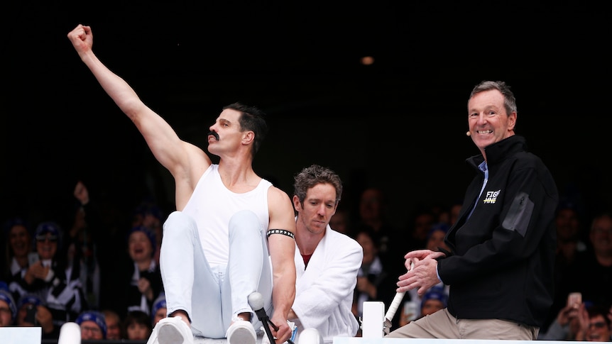 A retired AFL footballer dressed as Freddie Mercury prepares to slide into an icebath, as Neale Daniher smiles.