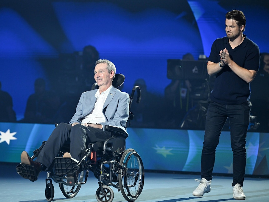 A man wearing a suit sits in a wheelchair on court at the Australian Open, in honour of his naming as Australian of the Year.