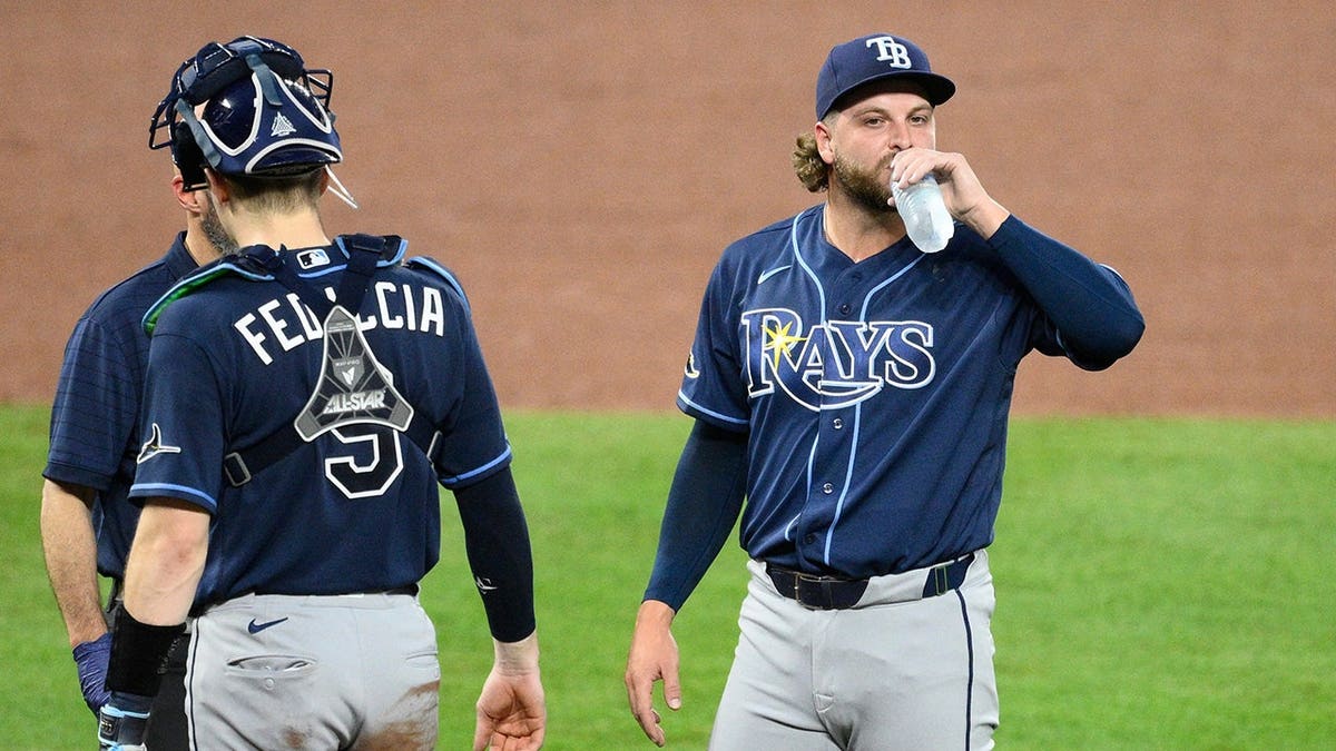 Jonathan Heasley drinking water next to Hunter Feduccia and manager Kevin Cash during a baseball game
