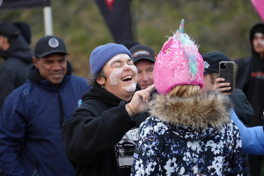 Jessi Rebel laughs as she helps apply face paint to a woman